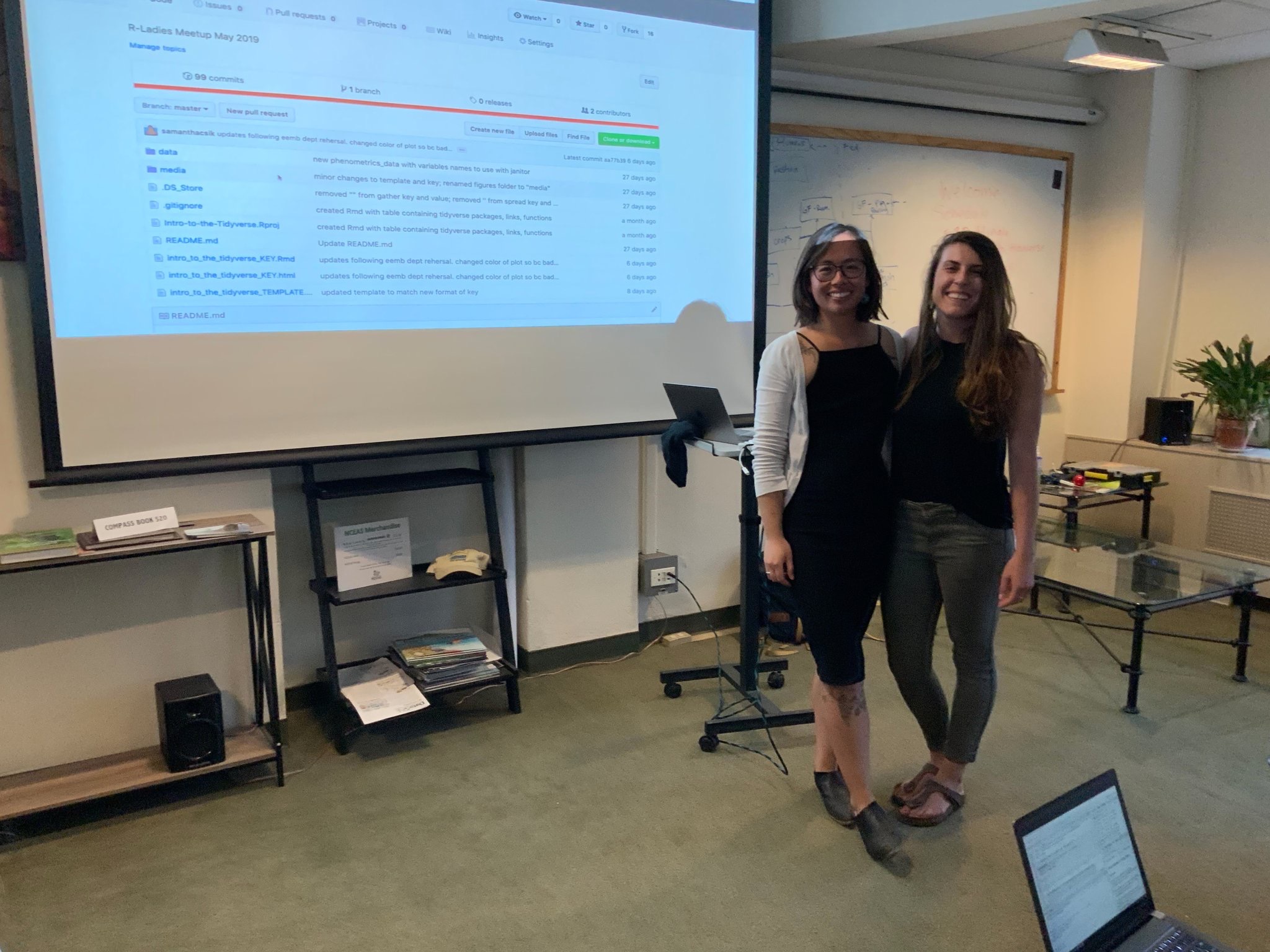 Two women, Sam and An, stand smiling in front of a projector screen with a GitHub repository on display.